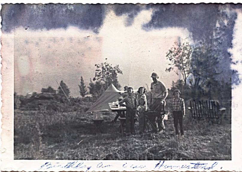 1959 July -Mother:  "Birthday on our Homestead" - on back:  "The clouds obliterated the mountains in back-ground.  This was about 7:00 in the evening" -- Probably Sharon's 4th birthday - I'm the one standing alone to my father's left - amazing for all the fire and water damage that the5 of us were so nicely preserved!