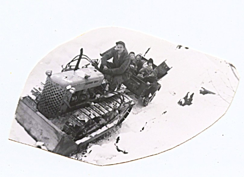 1960 April 3 Dad on Tractor in Snow - us in trailer - one way to get up the mountain - sometimes
